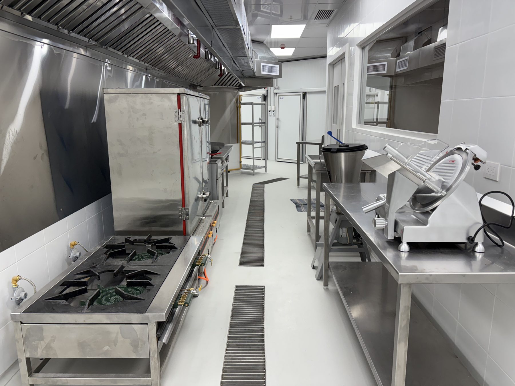 Cocina de Inbalnor: línea de cocción bajo campana, vaporera de gabinete a gas y mesas de preparación en acero inoxidable