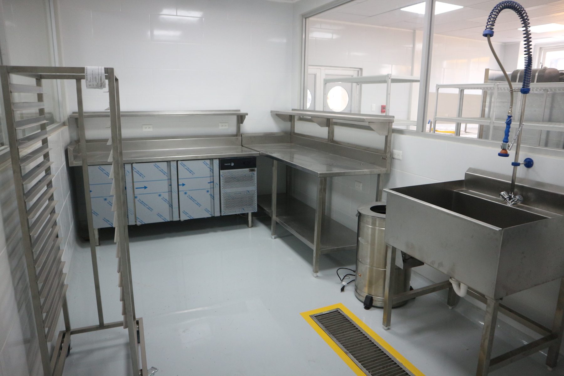 Área de preparación con mesa refrigerada, fregadero con ducha y carro de bandejas